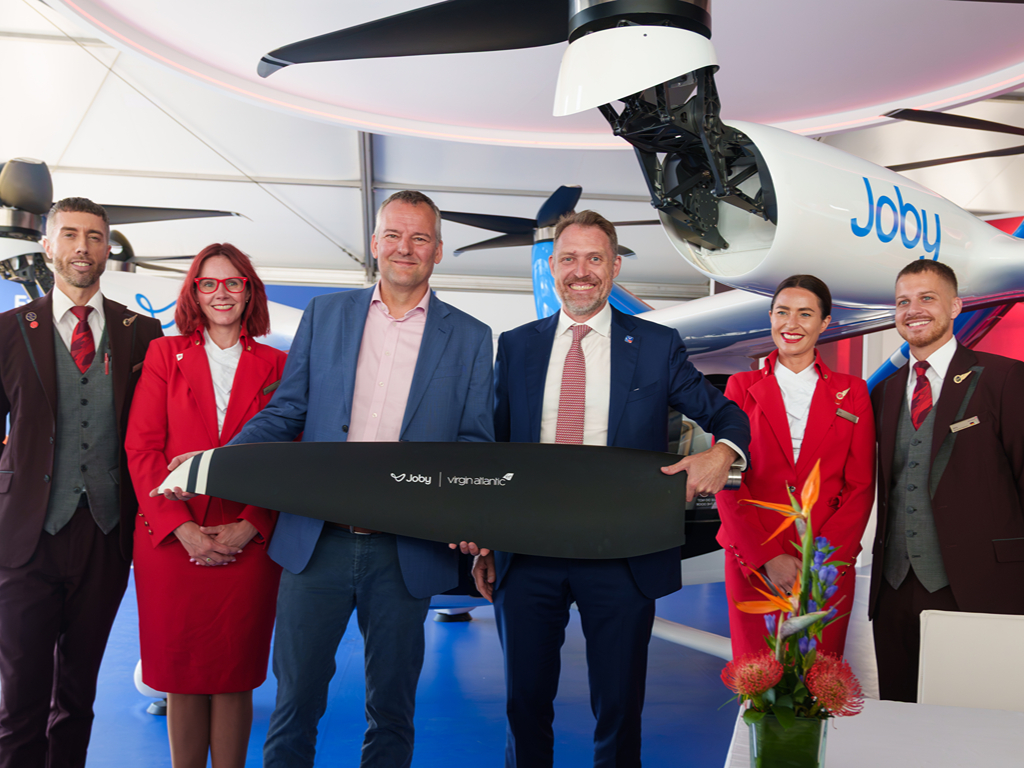 The CEOs of Virgin Atlantic and Joby Aviation hold a partnership sign, flanked by Virgin Atlantic crew